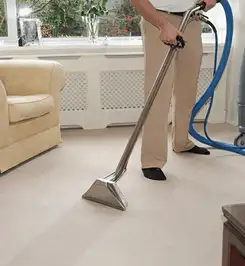 Professional carpet cleaner using a hot-water extraction wand and hose machine in a living room in Tucson, AZ.