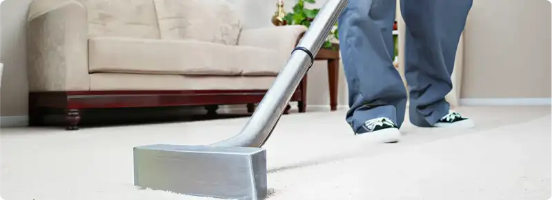 Carpet cleaning technician using a hot-water extraction wand on a light-colored carpet in a living room, Tucson, AZ.