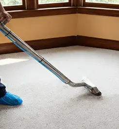 Steam carpet cleaning technician using a hot-water extraction wand on a residential carpet, wearing blue protective shoe covers Tucson, AZ.