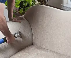 Professional upholstery cleaner deep-cleaning a fabric sofa with a handheld extraction tool and hose in Tucson, AZ.